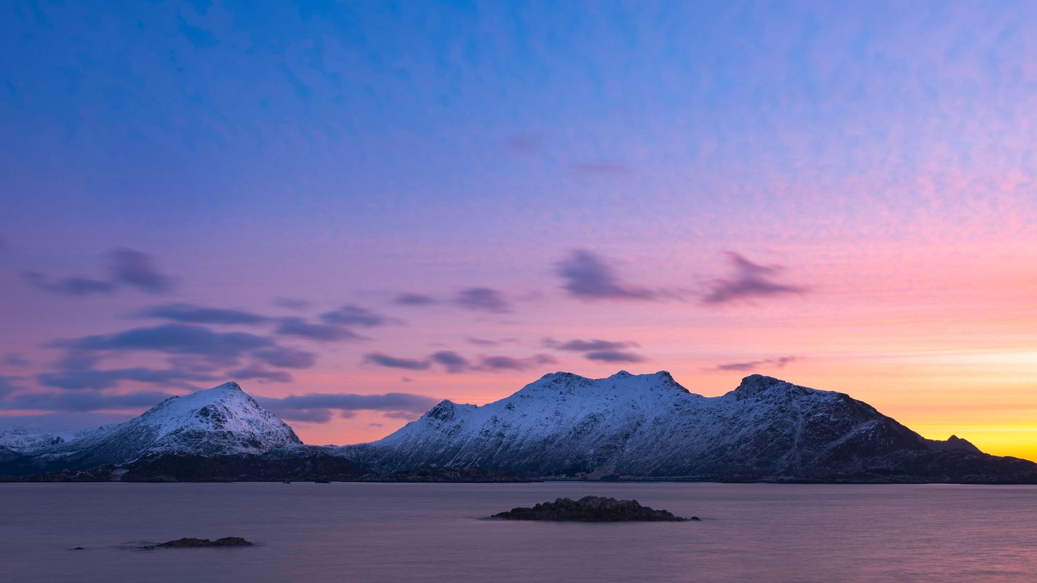 Mountain landscape transitions from daylight to sunset in panoramic view.