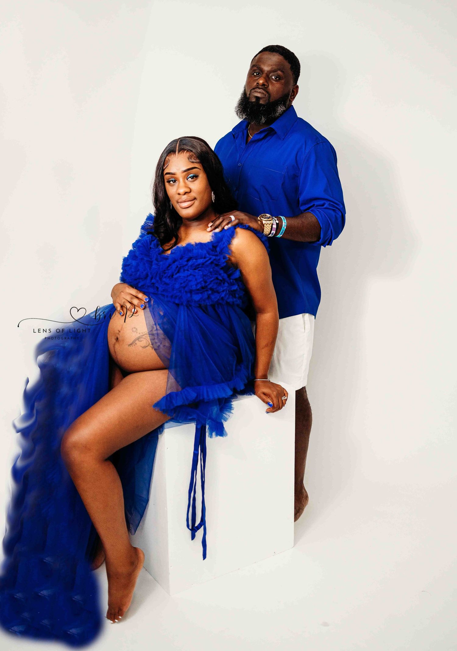 Couple in matching royal blue outfits pose for studio maternity portrait.