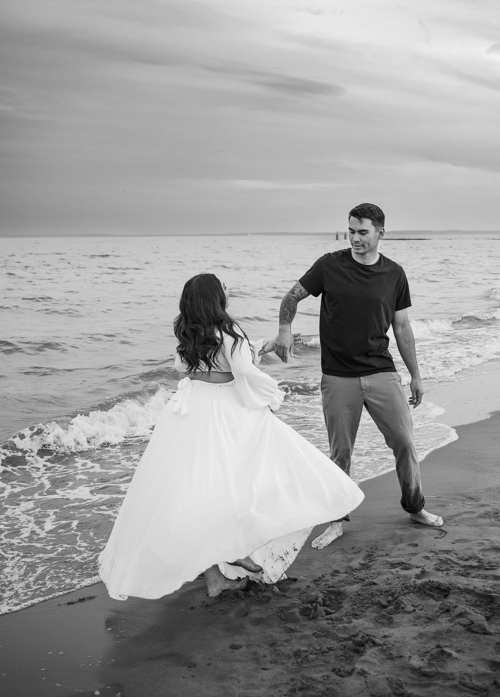 man twirling woman wearing flowing white gown in South Beach in Staten Island, NY