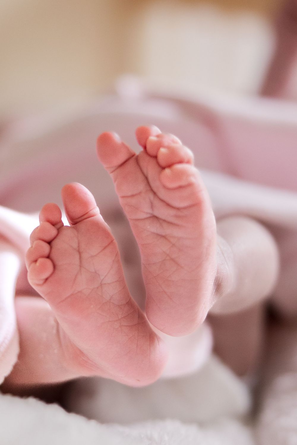 Close-up photograph of tiny newborn baby feet with delicate wrinkles and pink skin against soft white fabric.