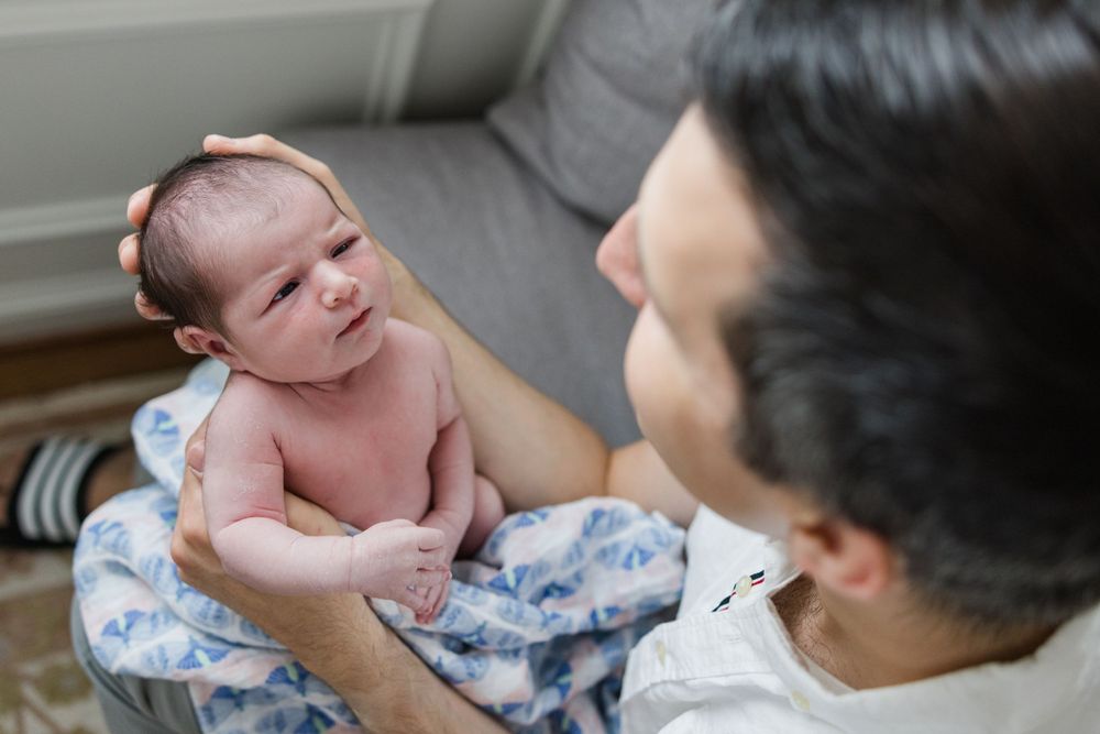 A newborn baby lies in her father's arms on a blue and white patterned blanket.