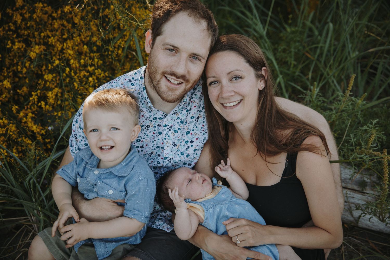 Family of four cuddled up smiling at photographer
