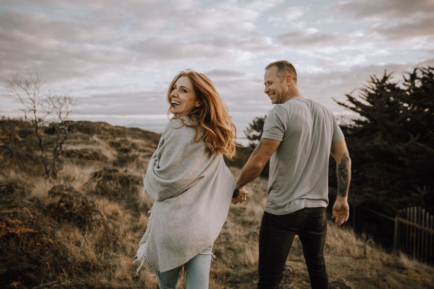 Girl being lead by boyfriend through grassy hill at sunset