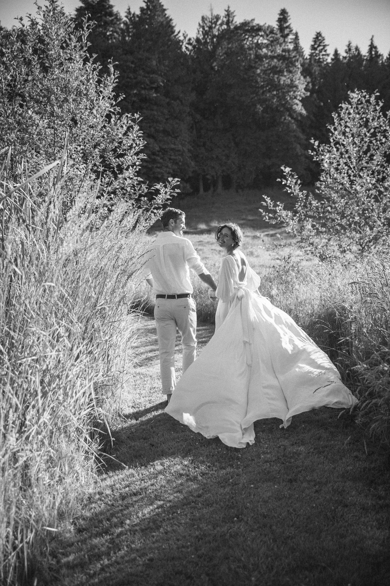Brides dress blows in the wind as she looks back and groom looks at her lovingly