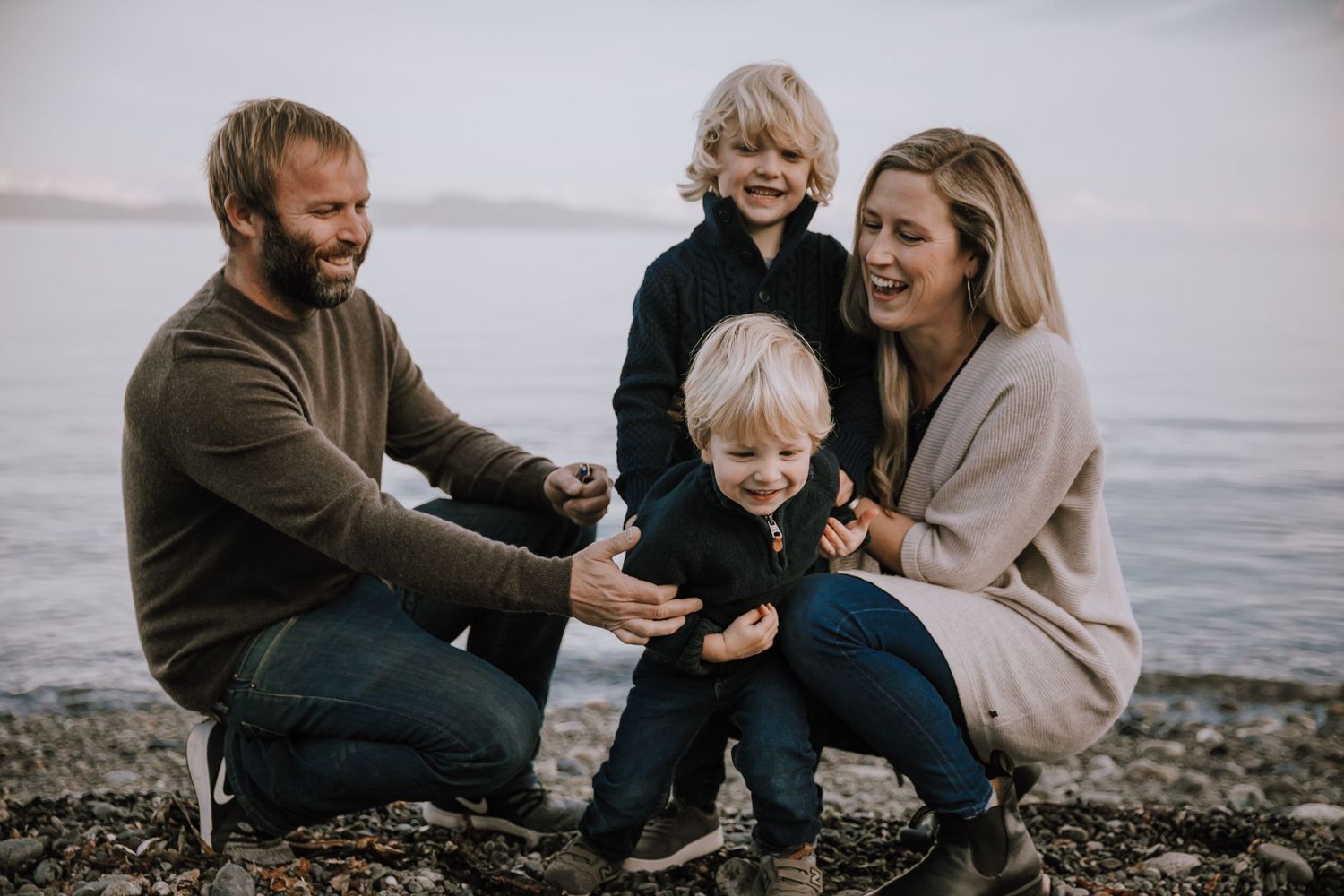 Family of four tickles youngest son on the beach