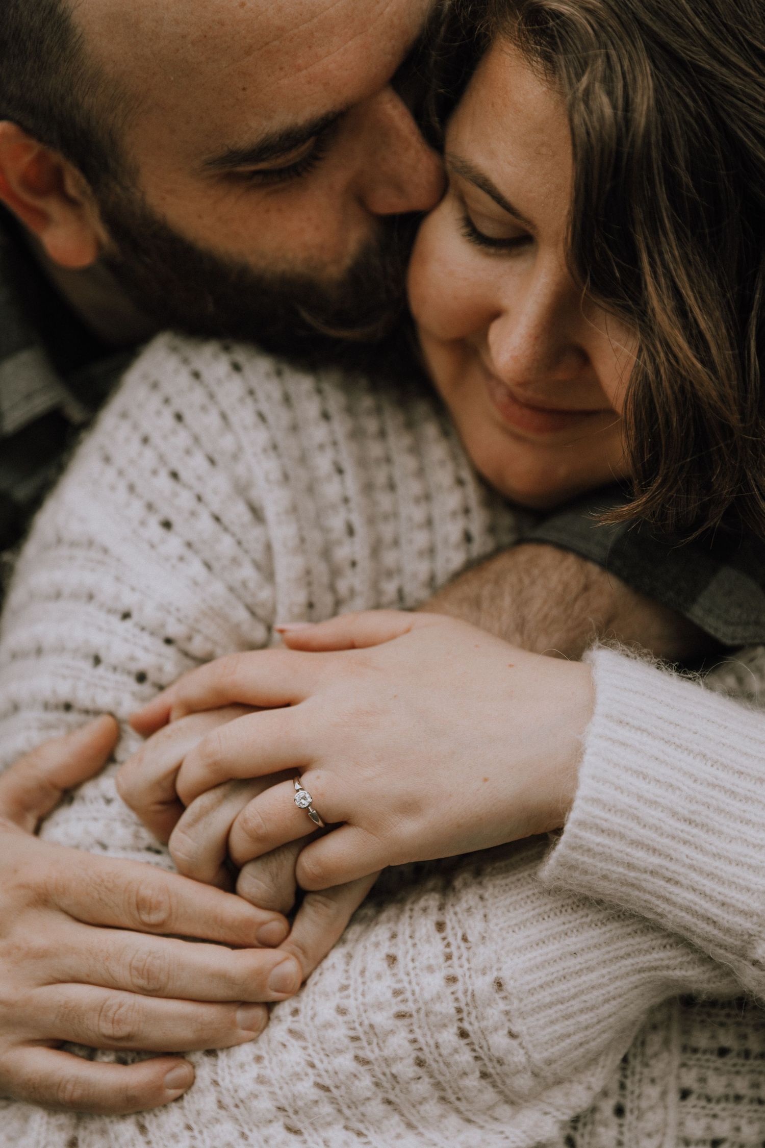 Engagement shot of ring while boyfriend gently kisses girlfriend's cheek