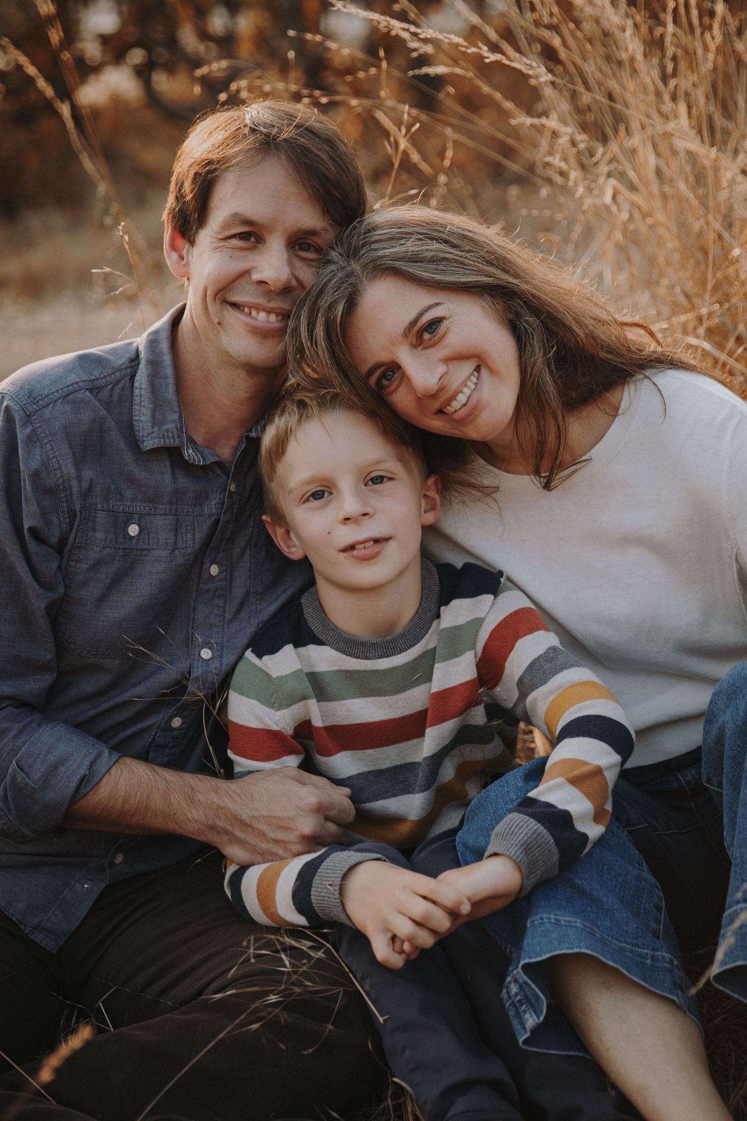 Family of three smiles in the golden grass