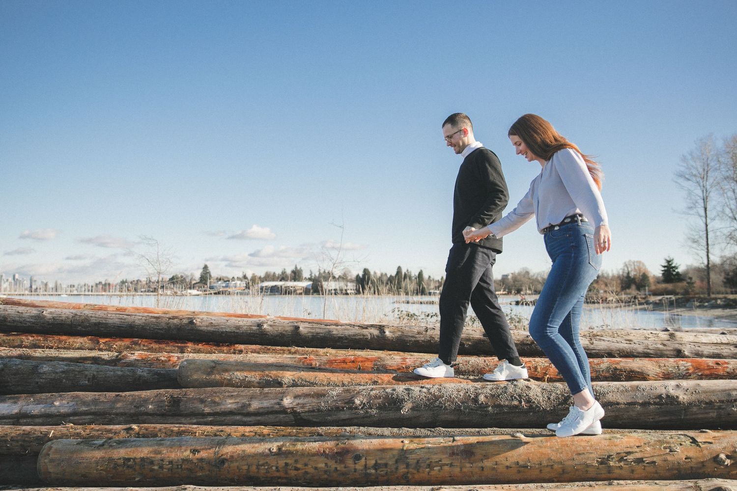 Engaged couple balance while walking along some logs
