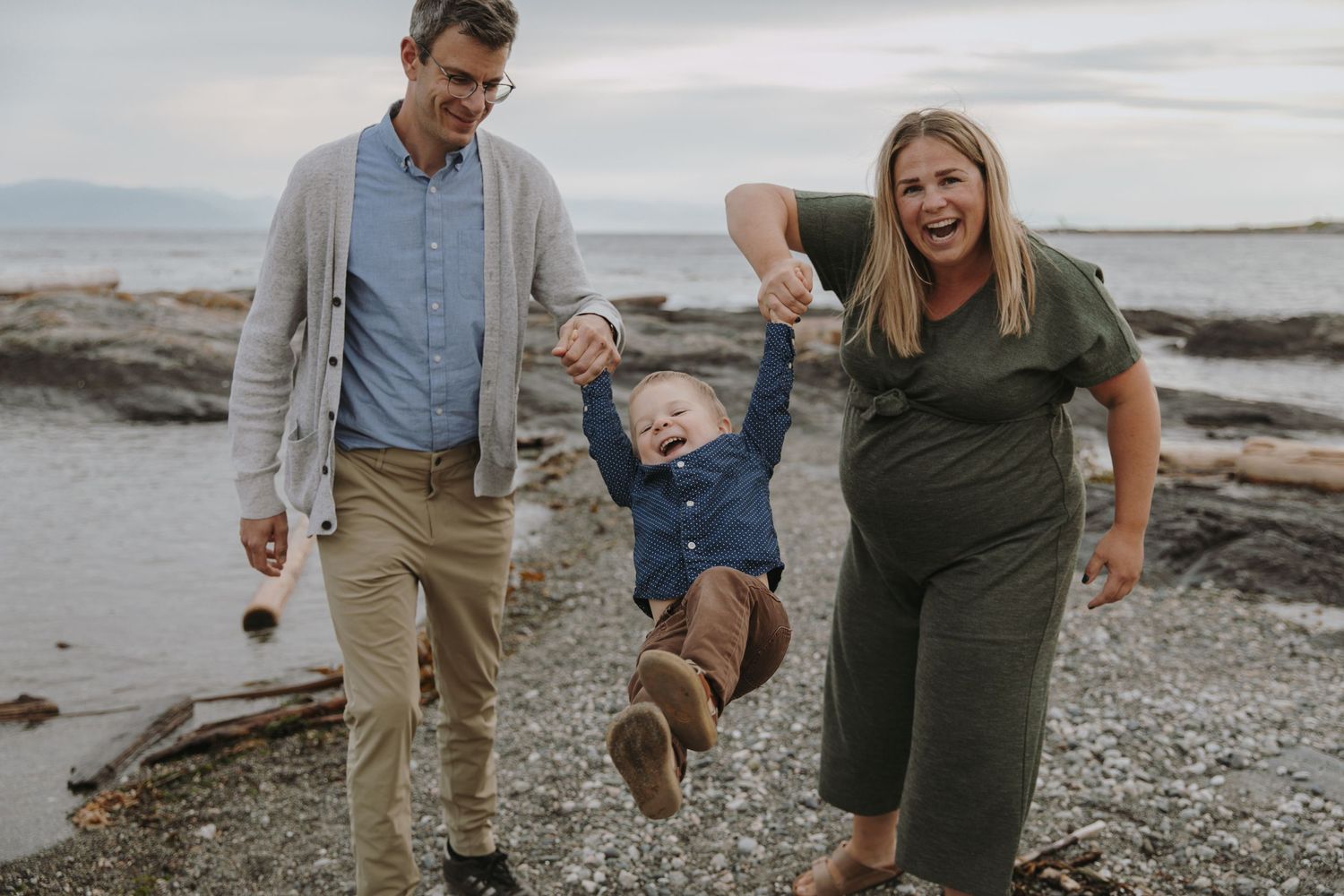 Pregnant mom and dad swing their young son with big smiles