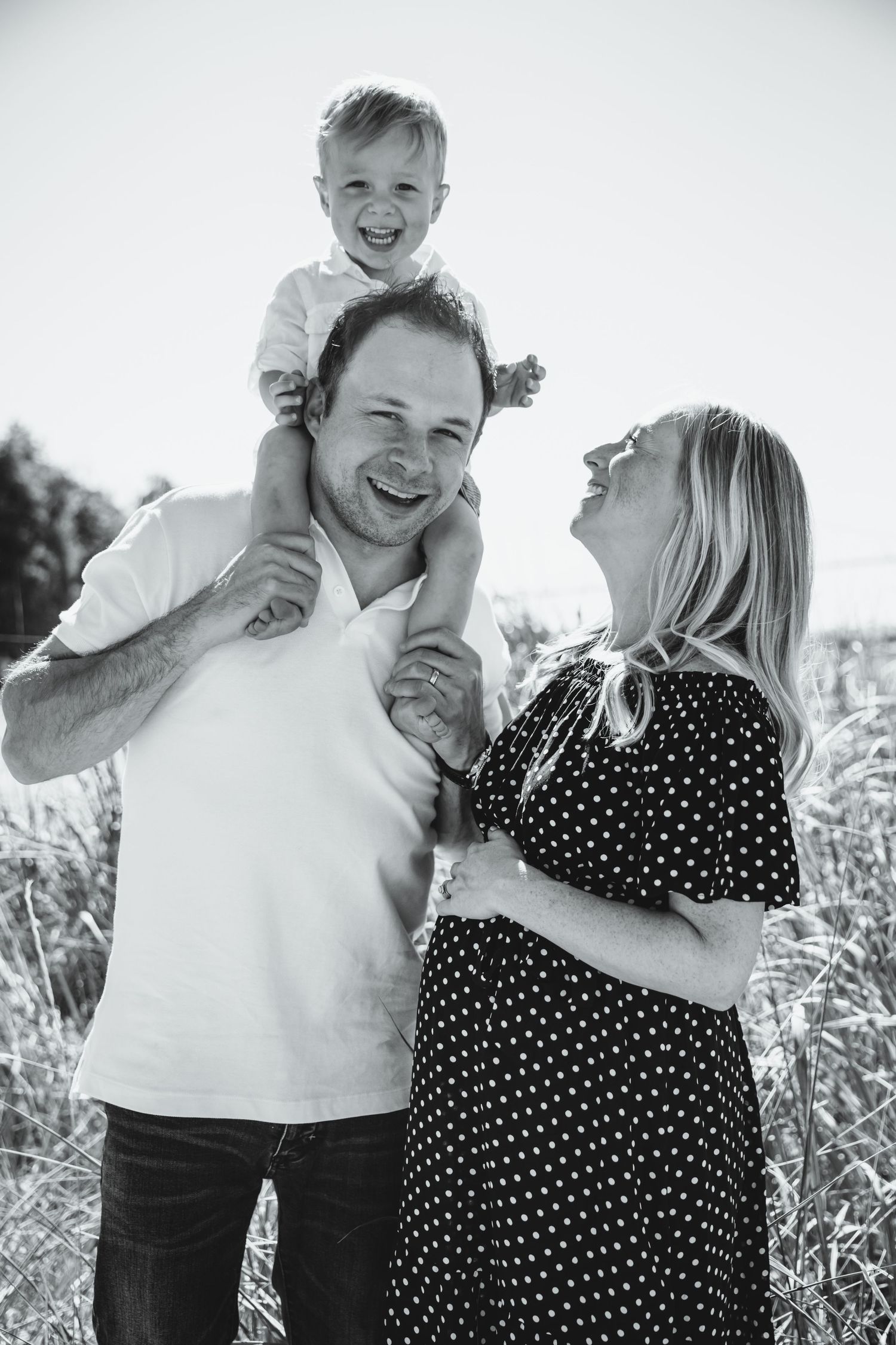 Son is on dad's shoulders while mom smiles up at him holding pregnant belly