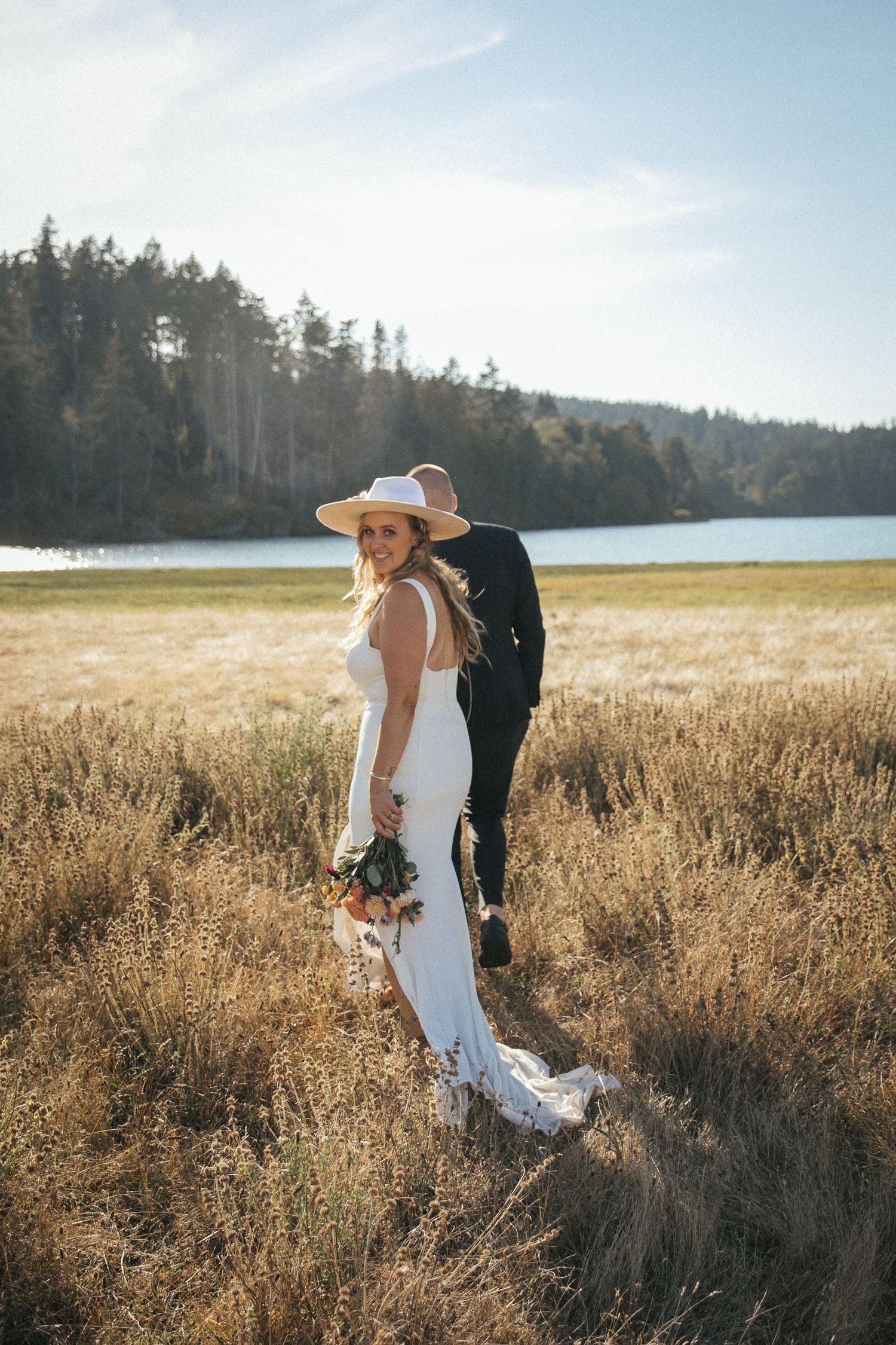 Bride looking back as couple walks towards the beach