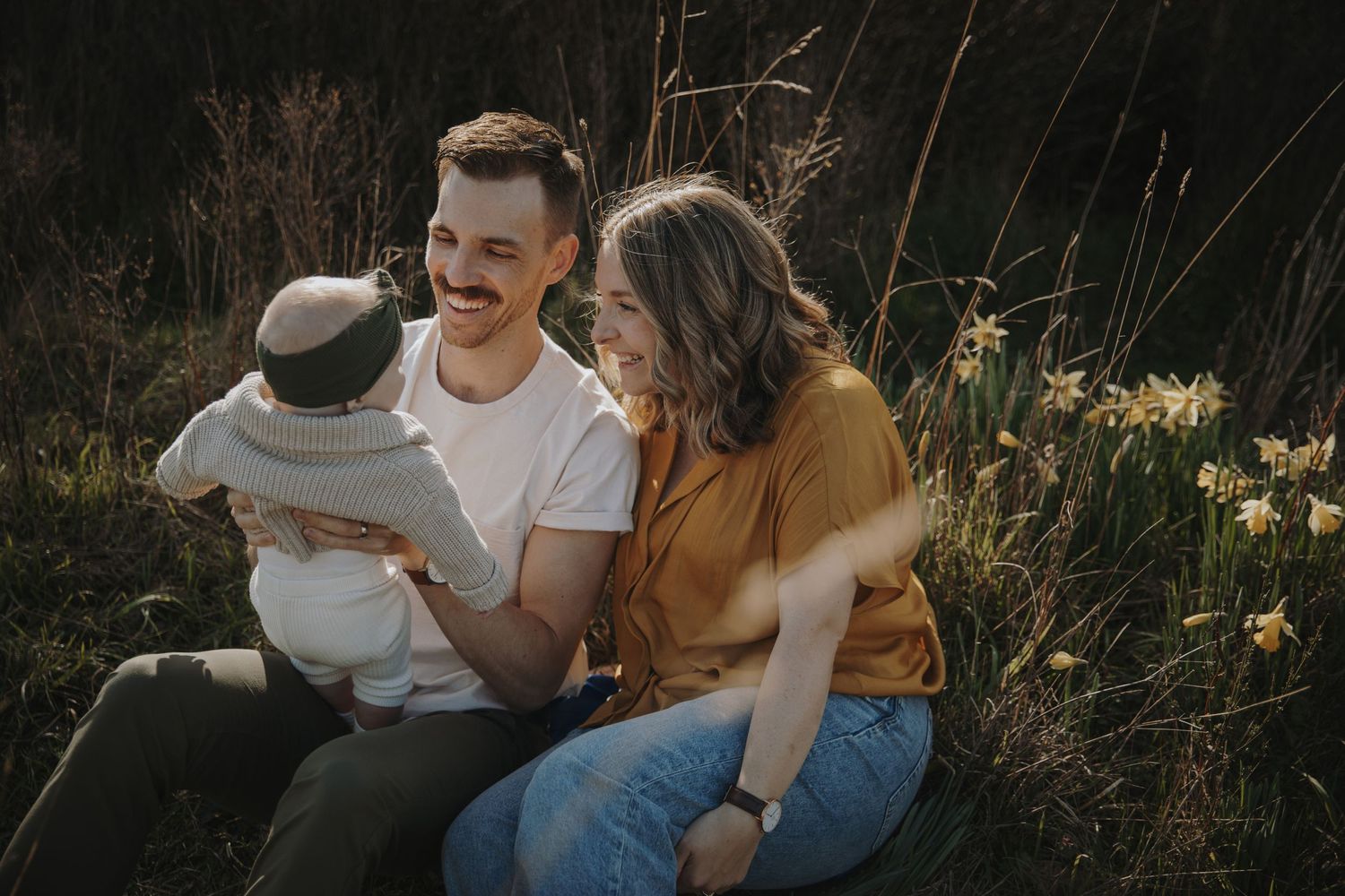 Family of three amongst the daffodils smiling at baby