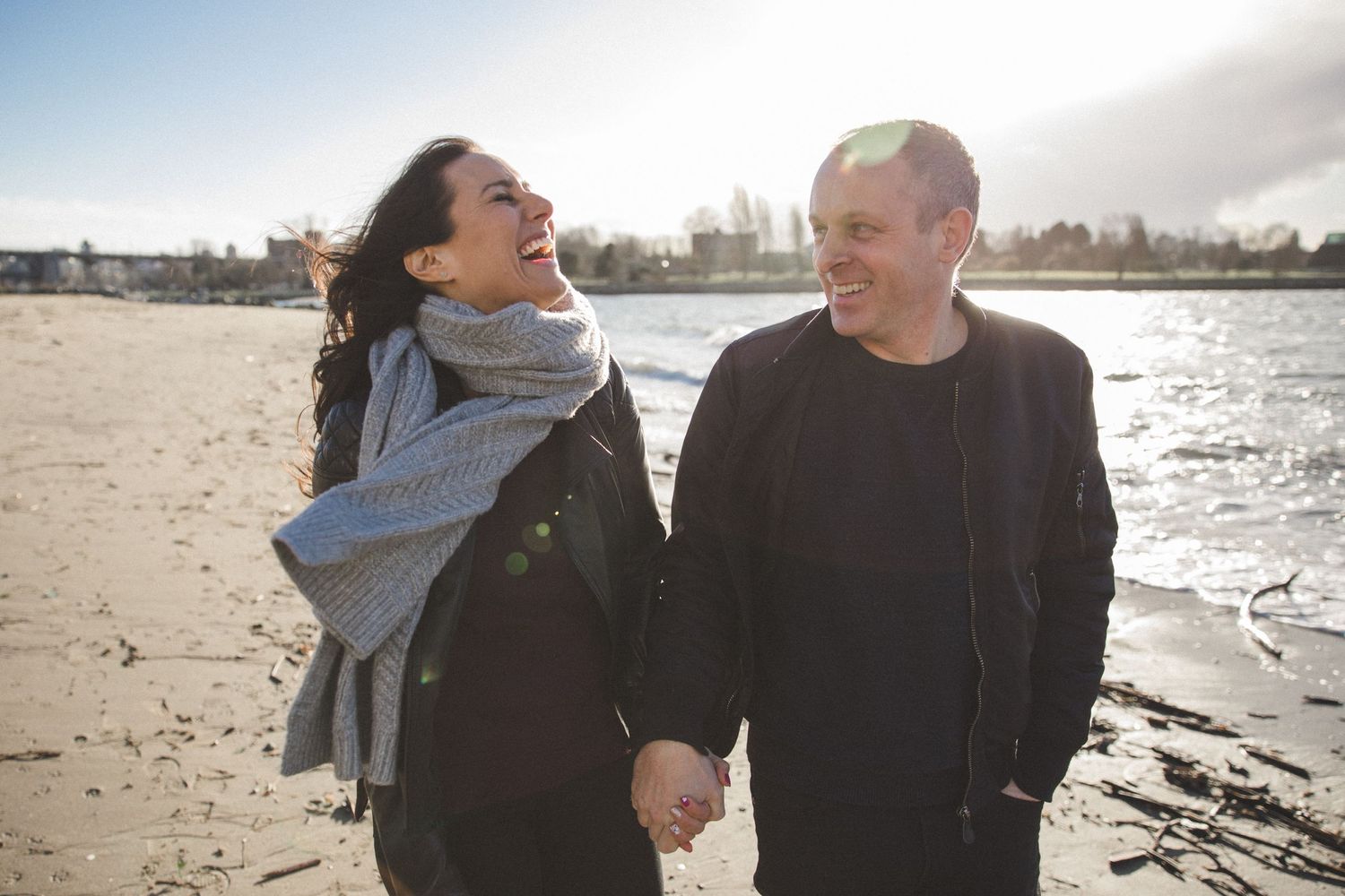 Couple walking along the beach while holding hands and laughing in the wind
