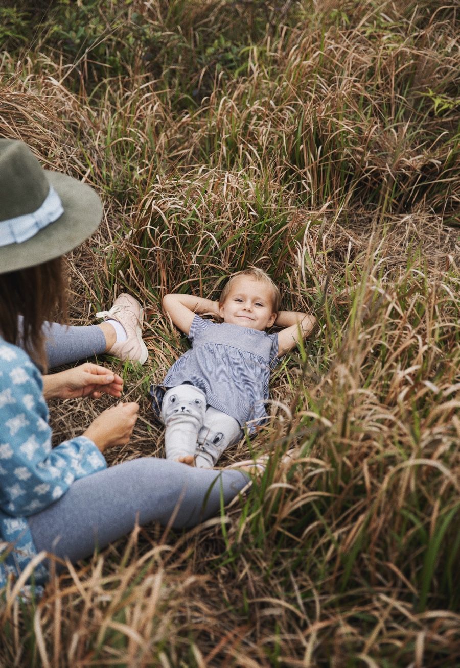 Little girl lying in the grass smiling while mom looks down at her