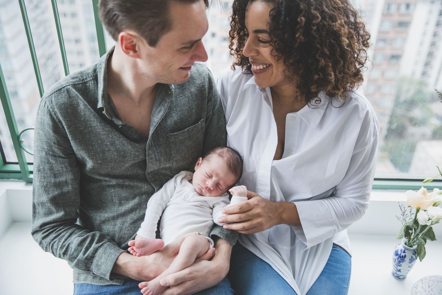 New mom and dad smile at each other while newborn sleeps in their arms