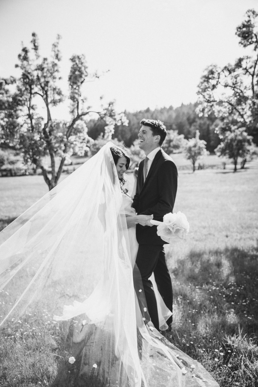 Bride and groom laughing as veil blows in the wind