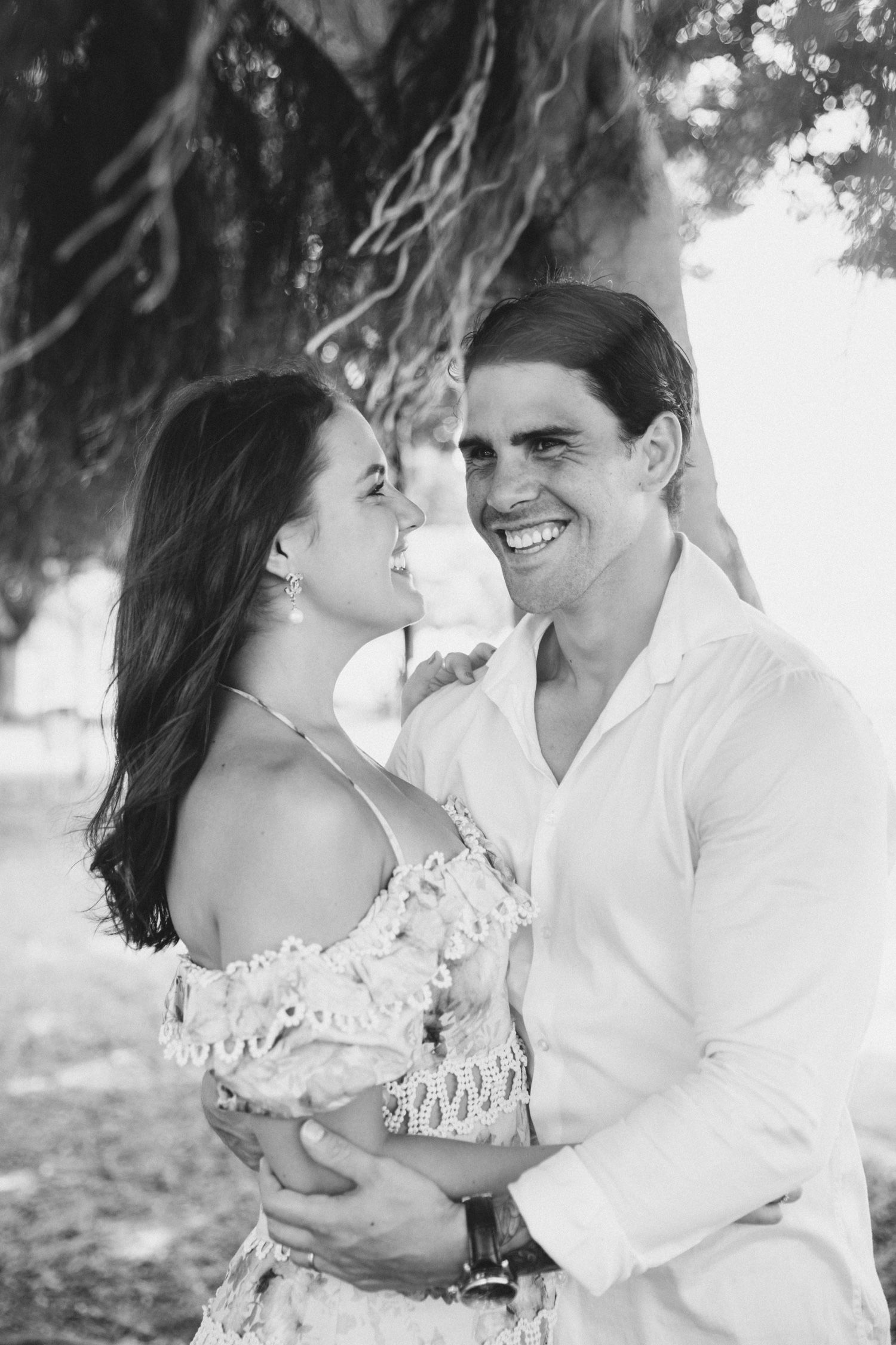 Couples smiles under tree while the wind blows