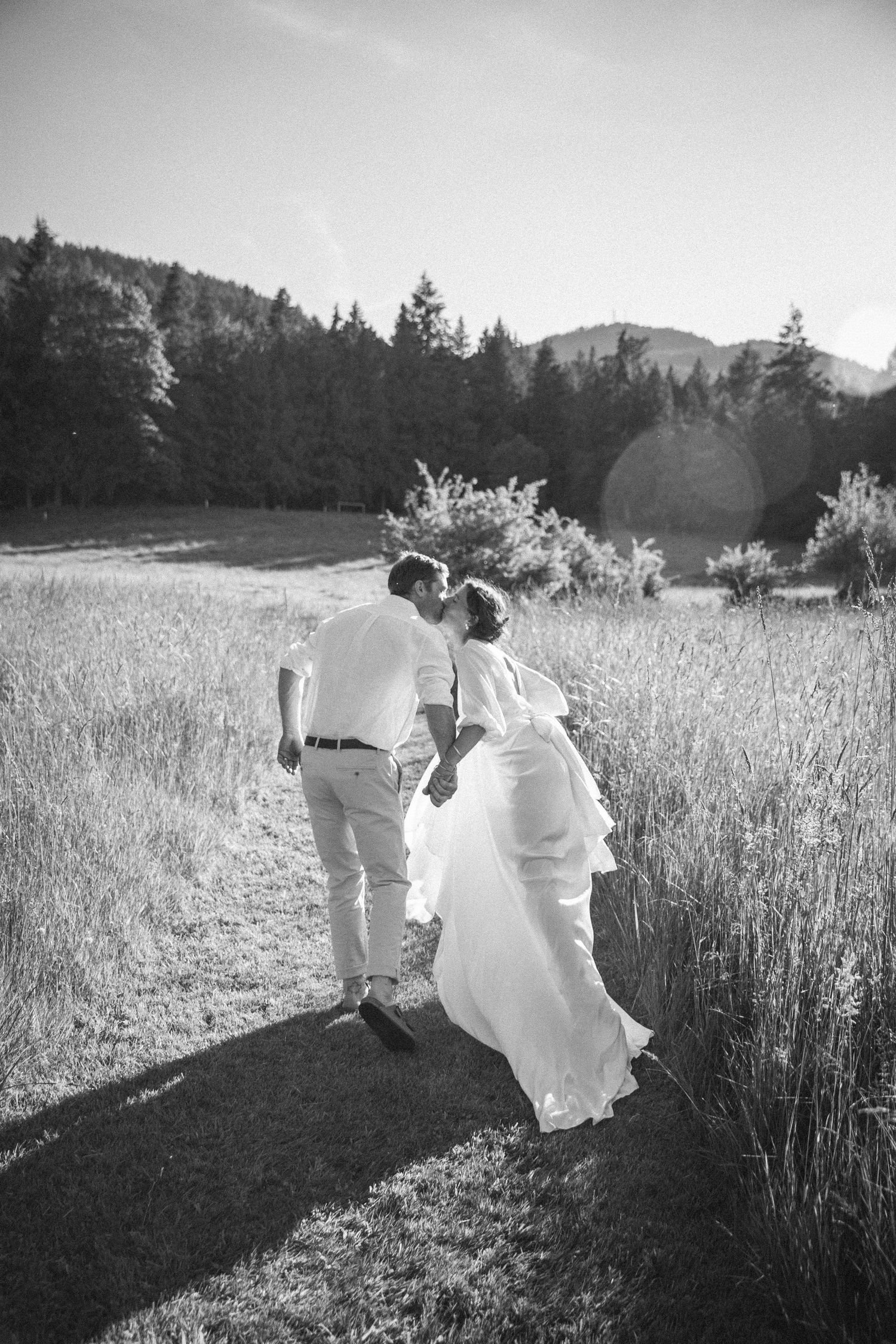 Bride and groom walking away while kissing at sunset in field