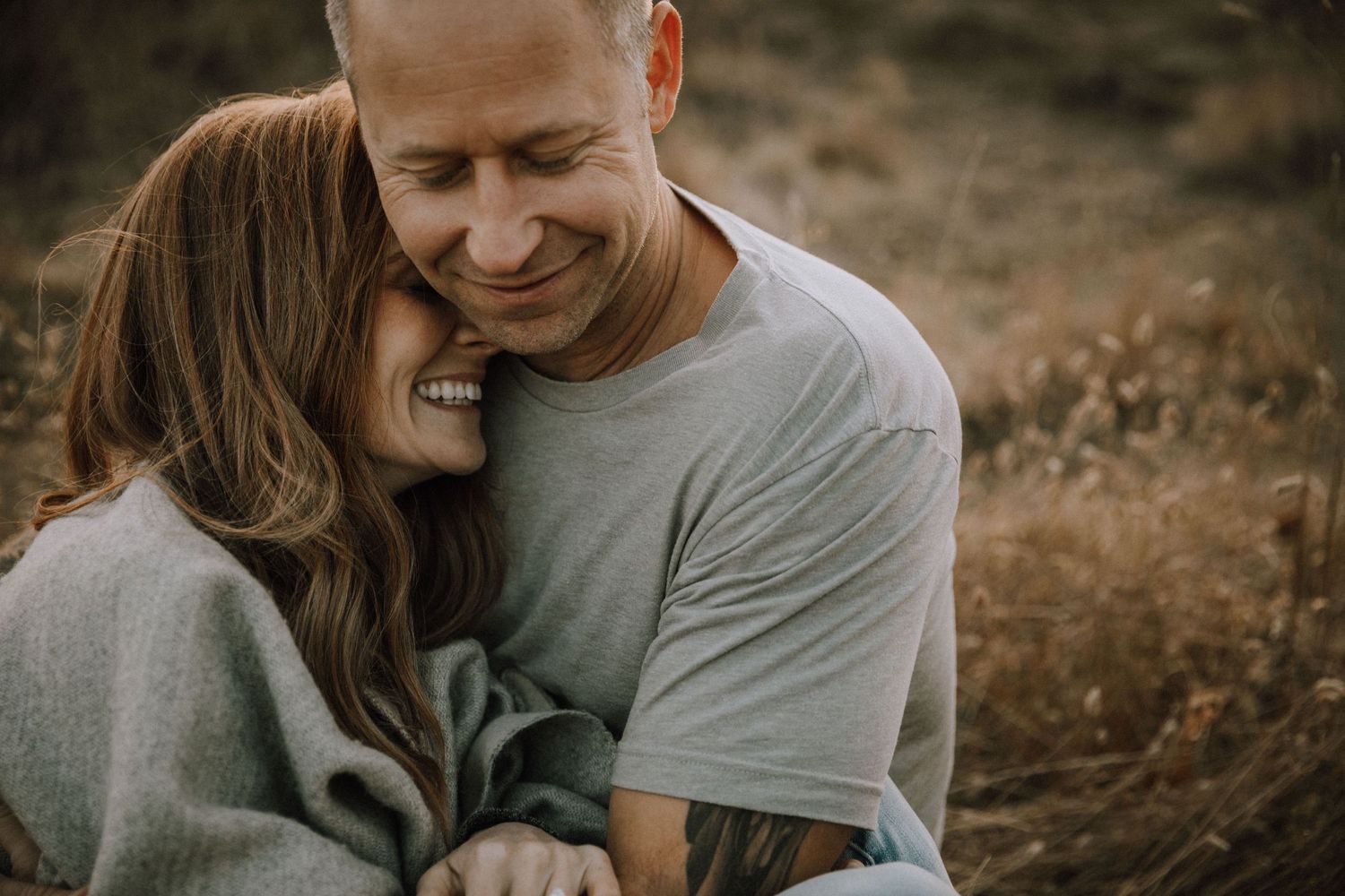 Girlfriend snuggling into boyfriend's neck in golden grass