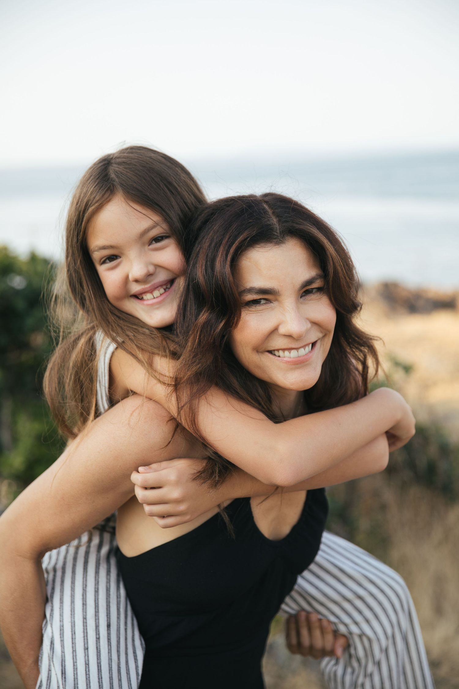 Mom gives daughter a piggy back while they both smile