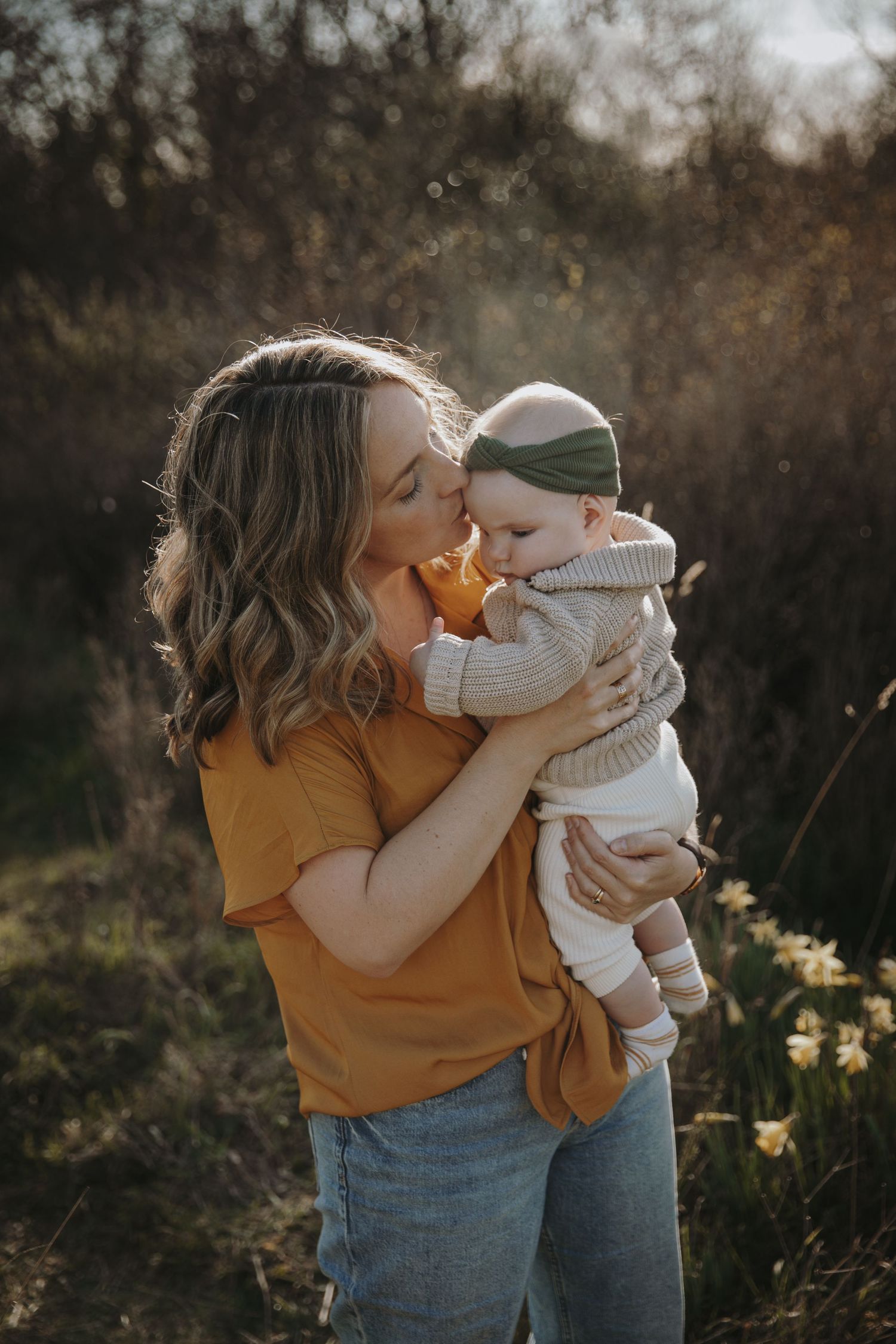 Mom kisses baby girl in field of daffodils
