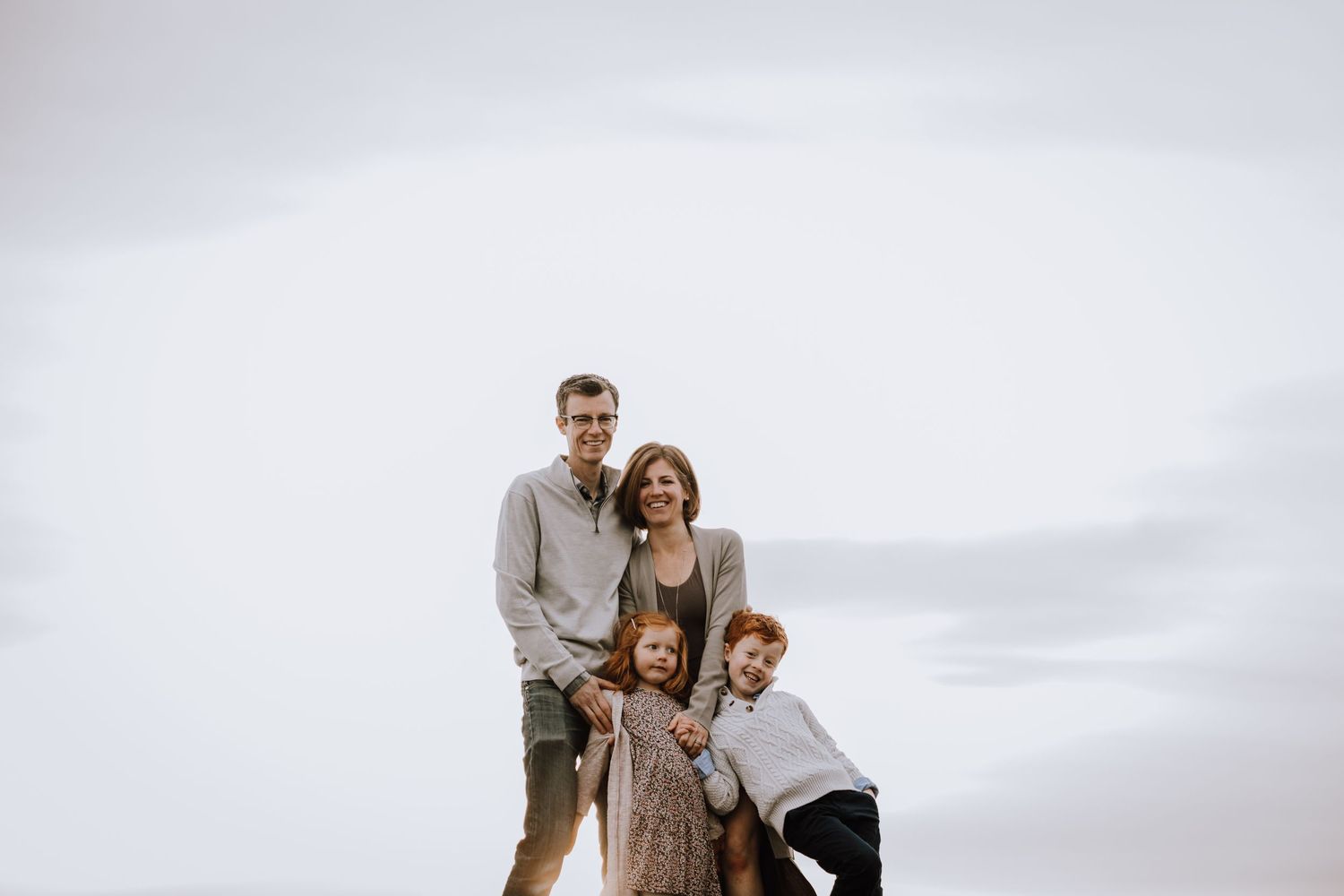 Family of four snuggles up on top of hill against white sky