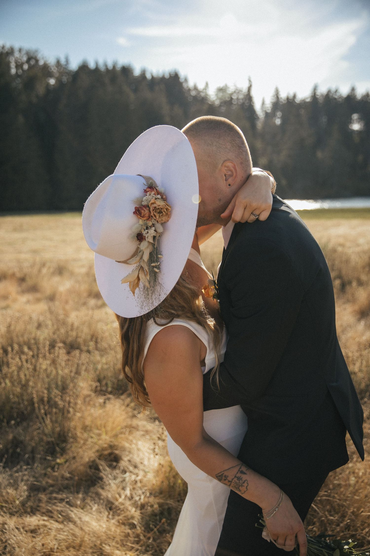Bridal couple sharing a kiss behind the brides hat at golden hour