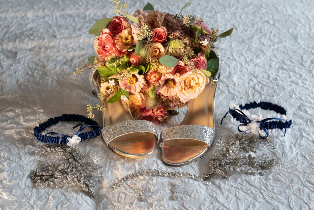 Wedding details featuring a peach and coral floral bouquet with matching bracelets and shoes on white lace.
