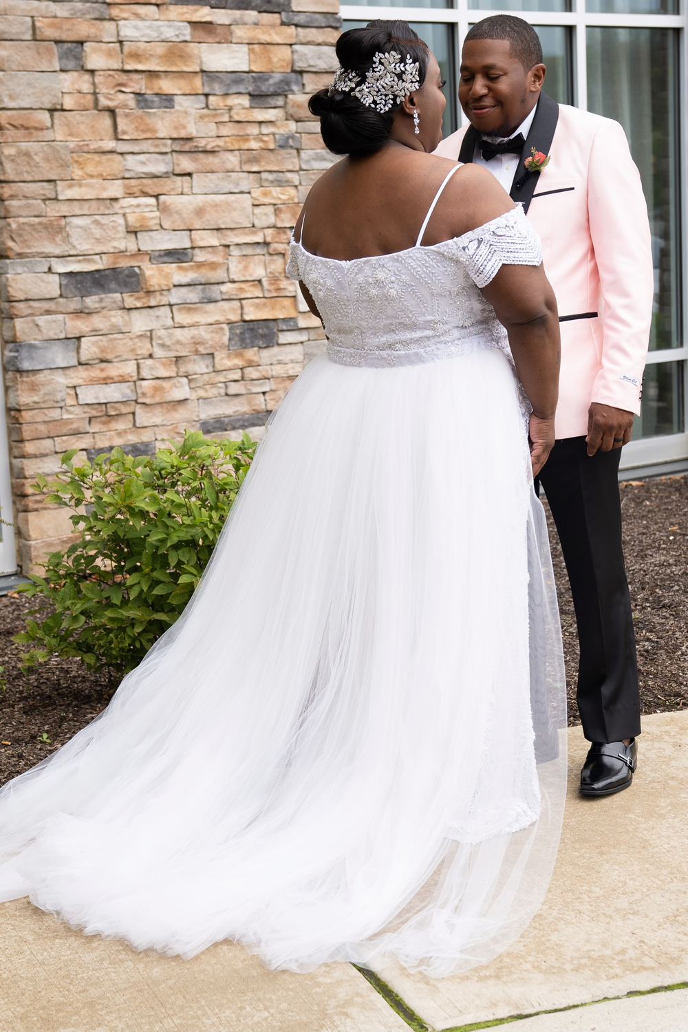 A bride and groom share a moment outside against a stone wall background.