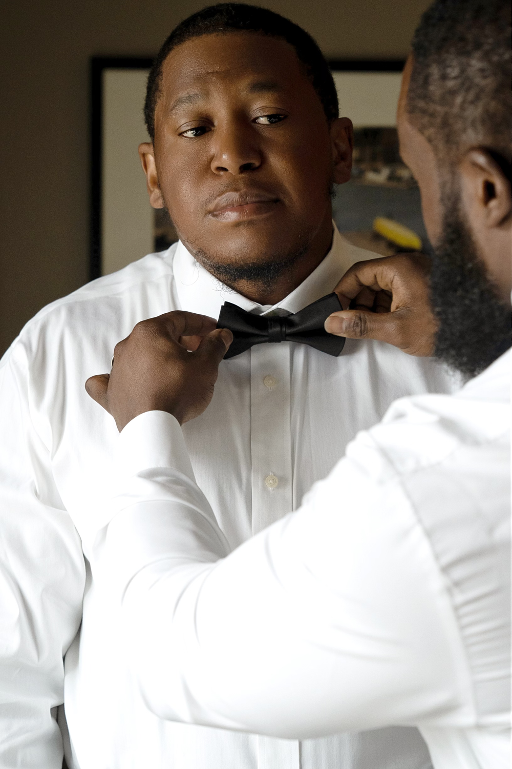 Someone adjusts a black bow tie in front of a mirror while getting dressed.