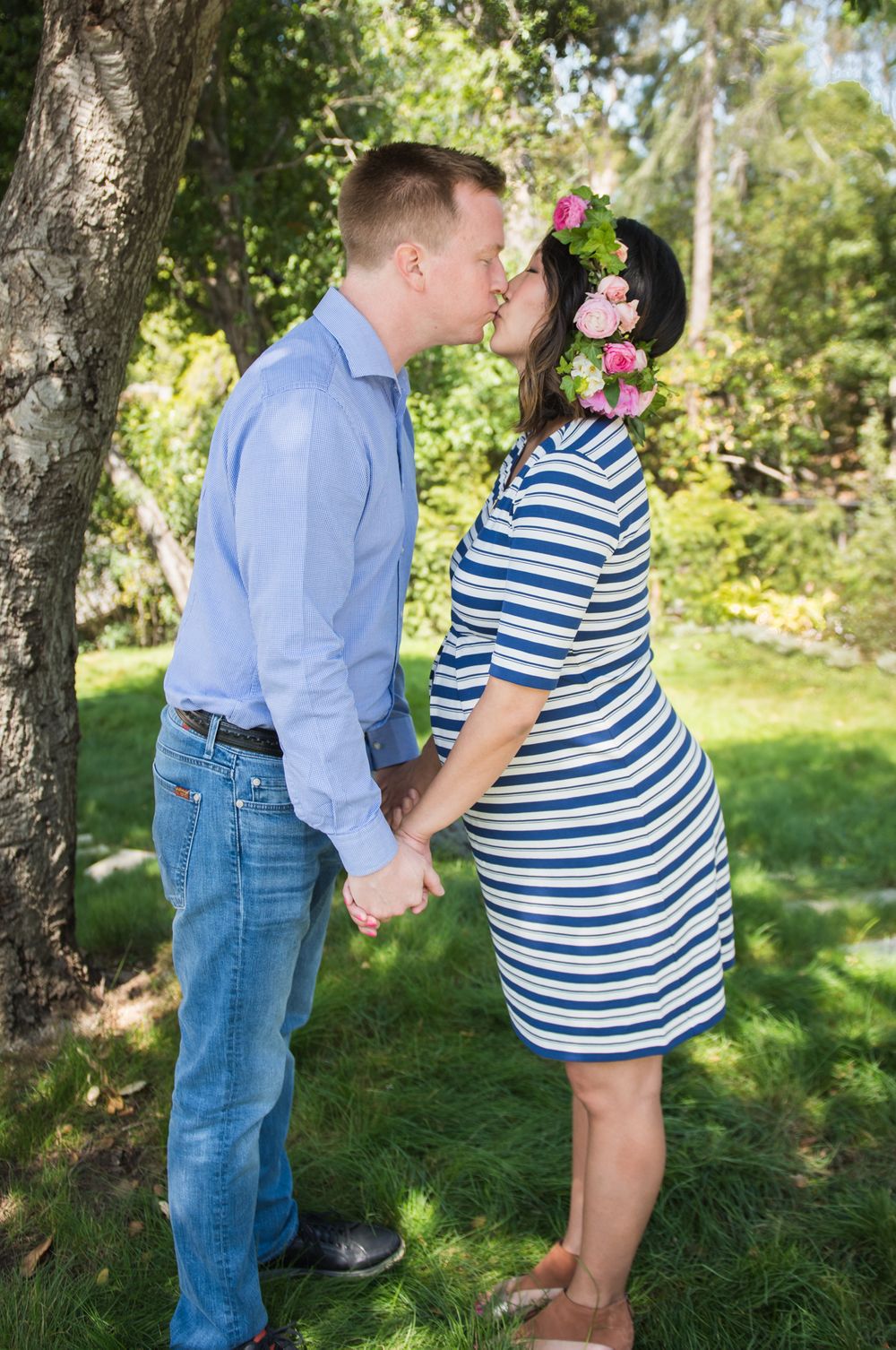 Romantic outdoor portrait of couple kissing under tree with pink floral crown.