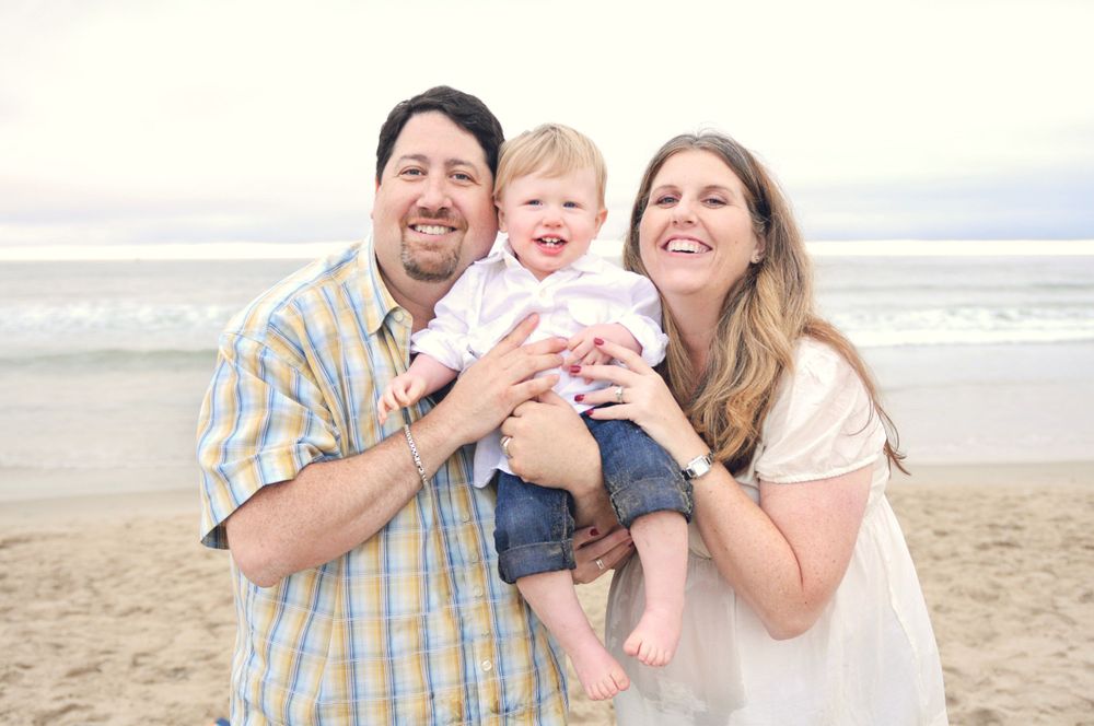 Happy family portrait at beach during sunset with toddler in casual attire.