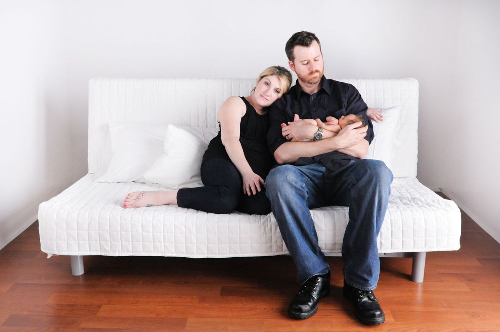 Two adults and a baby cuddling together on a modern white couch in a minimalist room.
