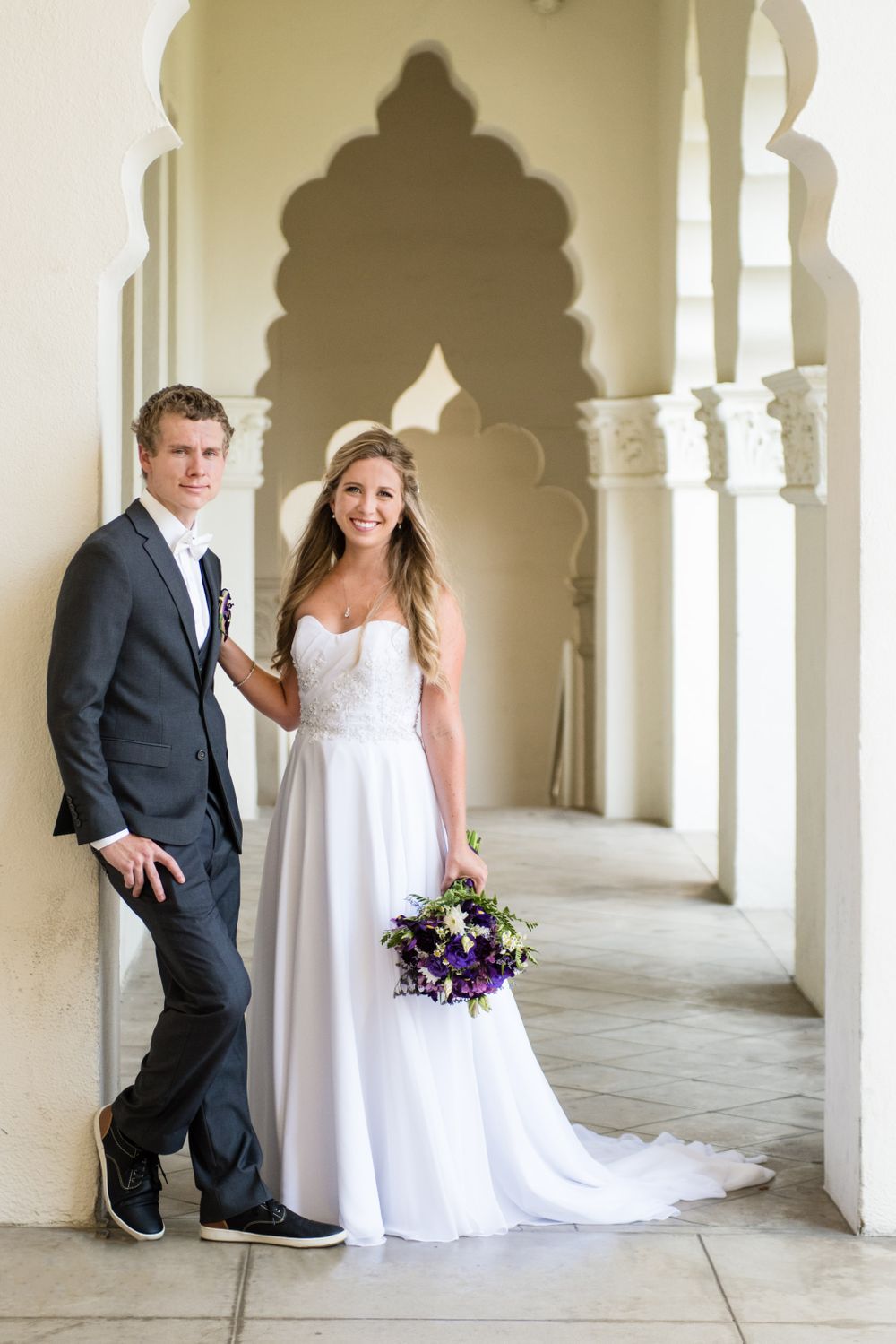 Elegant wedding photo of a couple posing under ornate archways in formal attire.