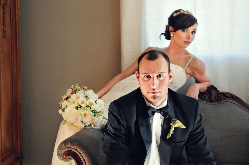 Stylish wedding portrait with couple in formal attire seated on vintage furniture.
