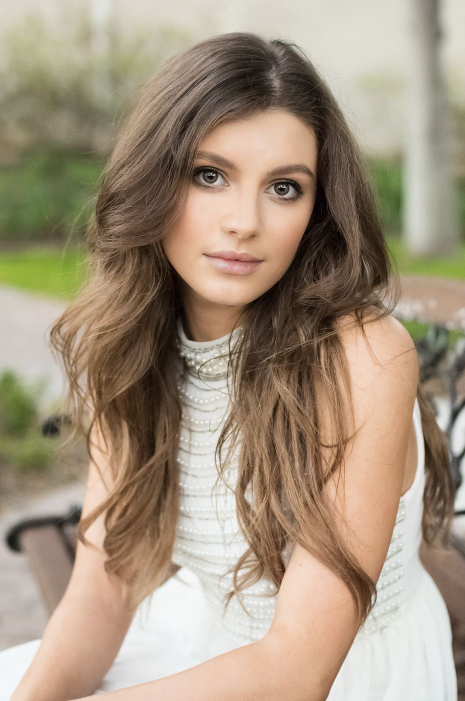 Portrait photo featuring long wavy brunette hair and white lace top in outdoor setting.