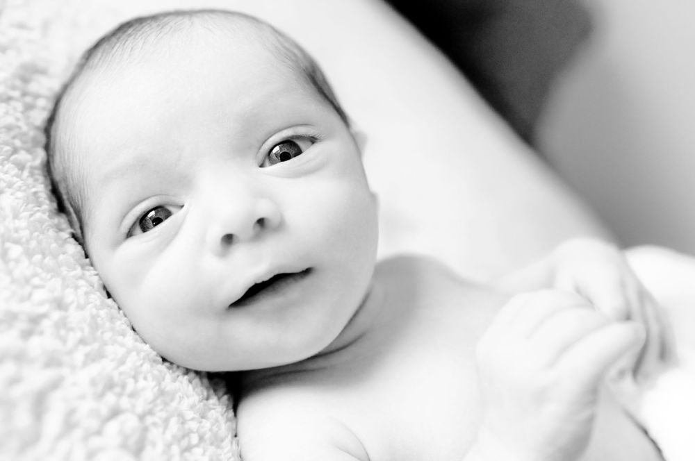 Close-up black and white portrait of a smiling baby with bright eyes lying on soft fabric.