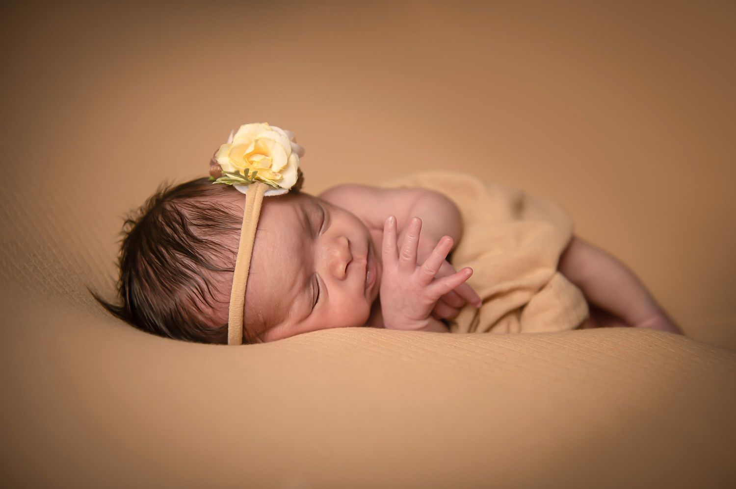 Peaceful newborn photography on warm brown backdrop with minimalist styling.