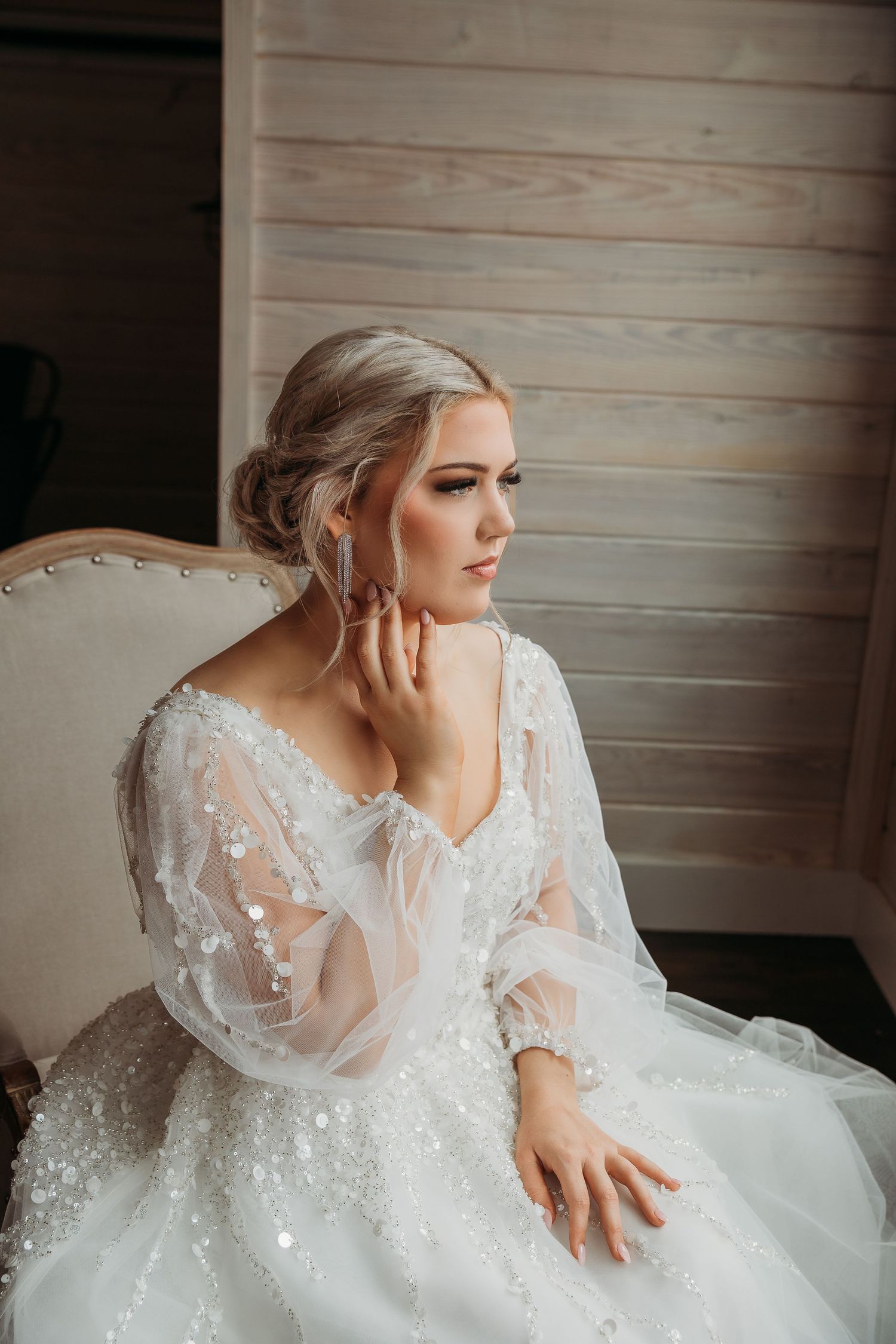 Elegant bride in lace wedding gown posing against rustic wooden wall.