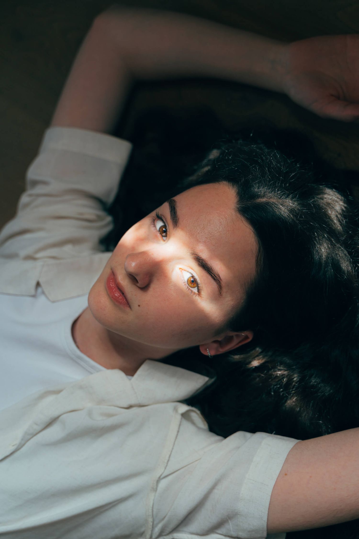 Portrait of someone in white clothing lying down with soft lighting.