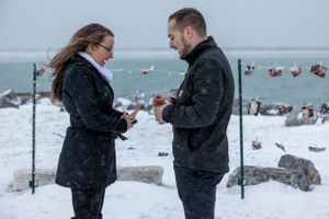 A winter engagement scene with two people exchanging rings in the snow.