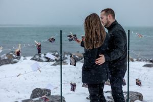 A tender moment between two people against a snowy coastal backdrop with decorative lights.