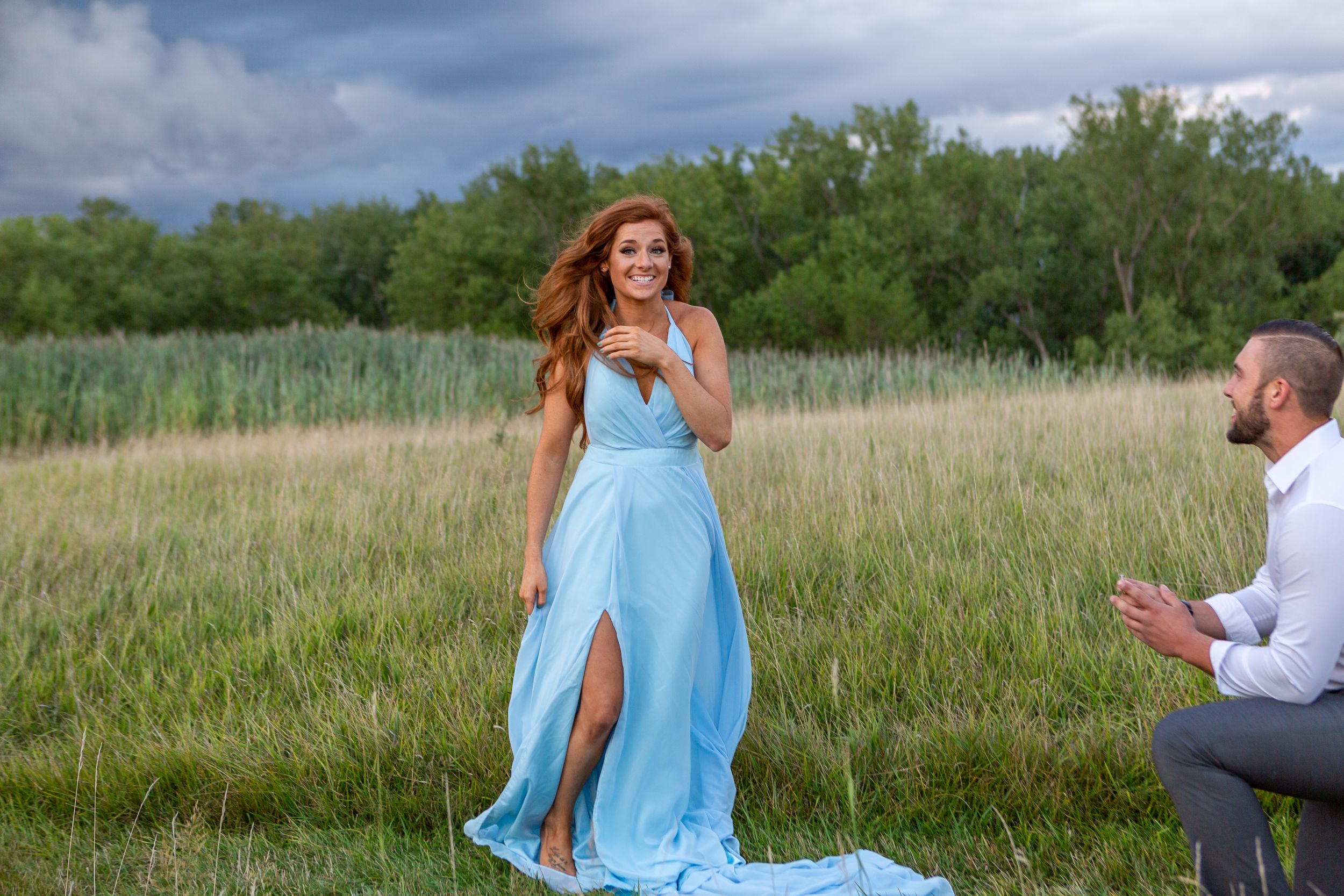 A surprise proposal moment captured in an open field with stormy skies above.