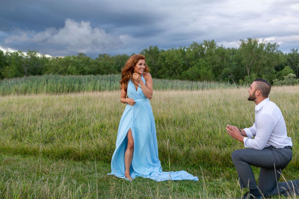 A romantic proposal taking place in a natural meadow setting with dramatic clouds.