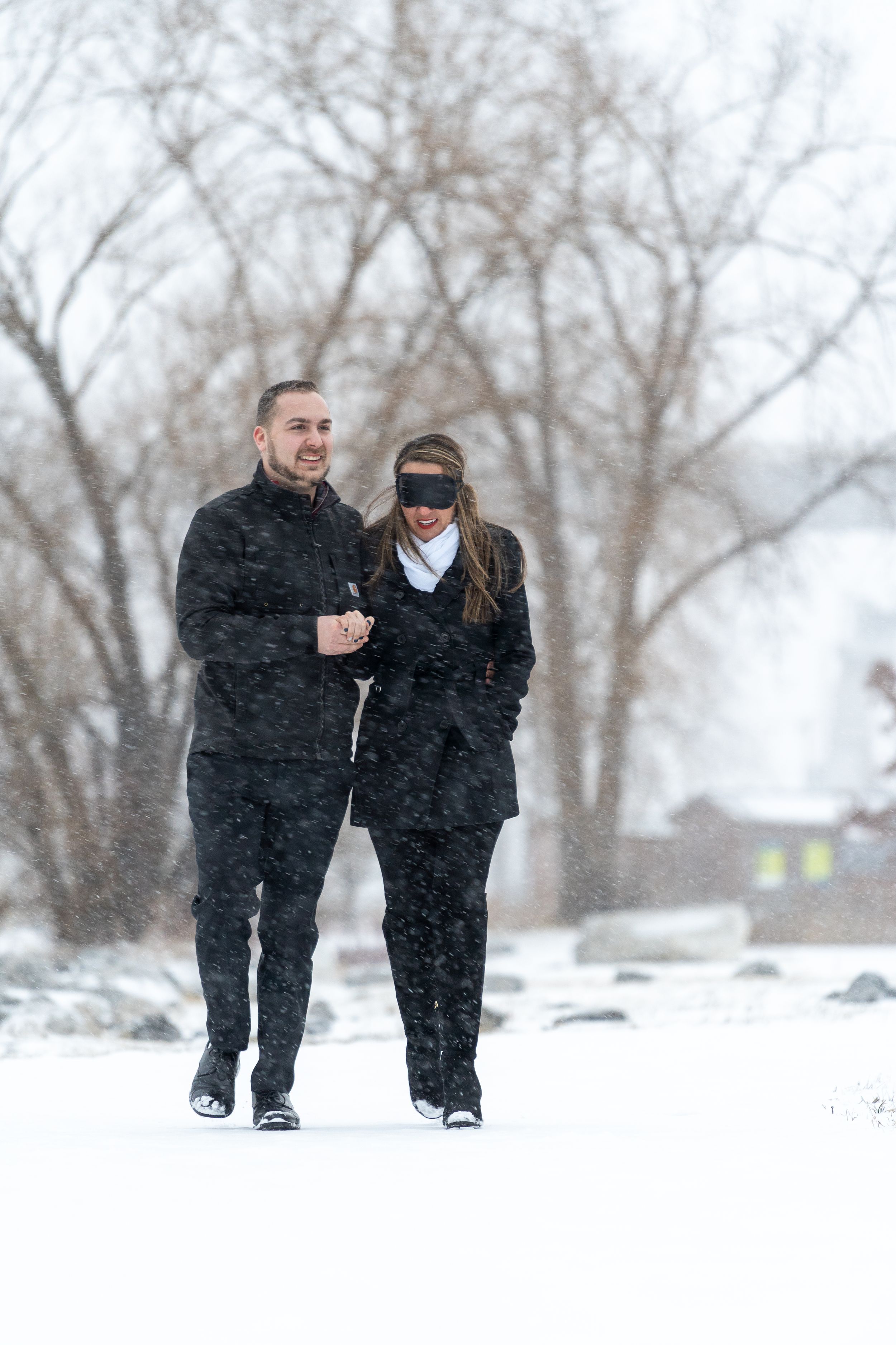A couple walks together through falling snow on a winter day.