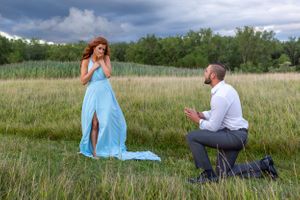 An emotional marriage proposal captured in a wild grass field under stormy skies.