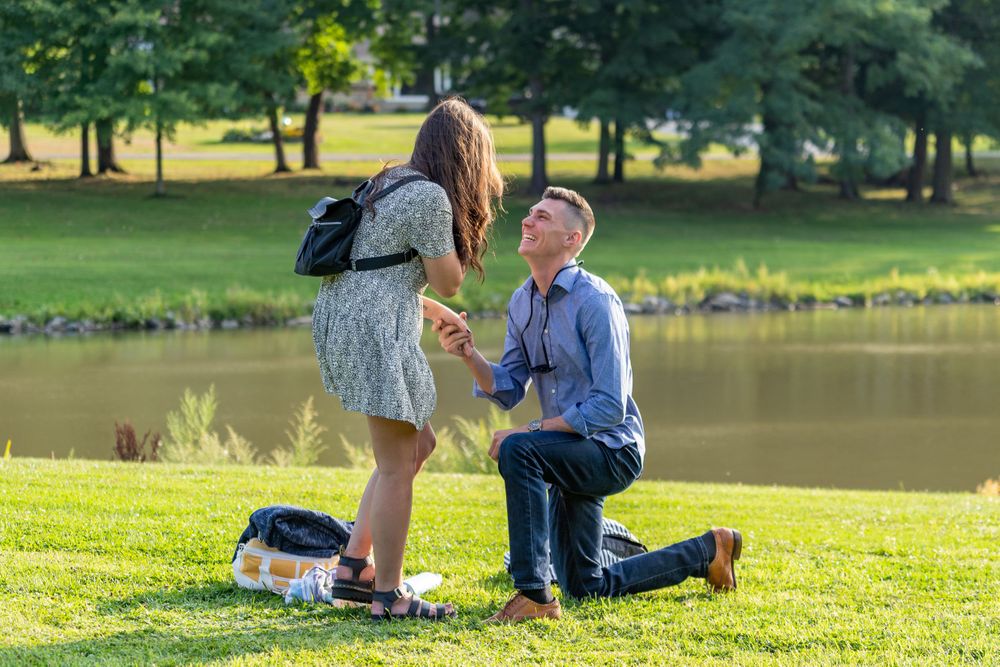 A couple shares an intimate proposal moment by a serene lake on a sunny afternoon.