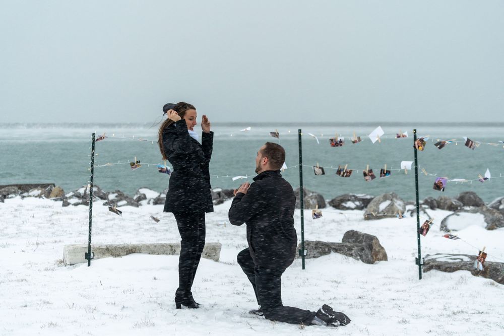 A romantic winter proposal scene with snow-covered rocks and ocean backdrop.
