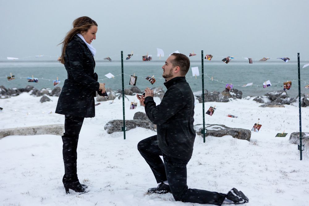 A romantic proposal moment captured in a snowy coastal setting with string lights.
