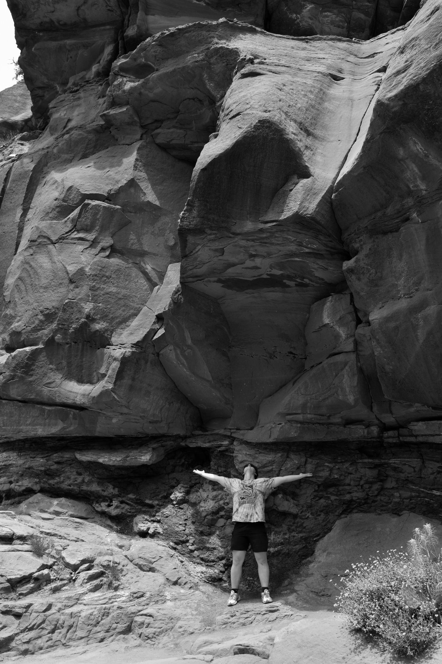 Figure stands with arms spread wide against massive red rock canyon wall.